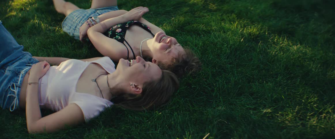 The girls laugh together while laying on the grass