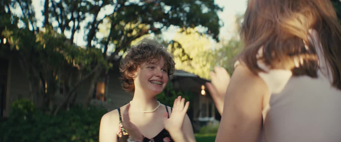 Girl smiles while clapping hands with another person outdoors