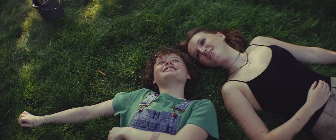 Teenagers lying on the grass share a relaxed moment under natural light in an outdoor setting