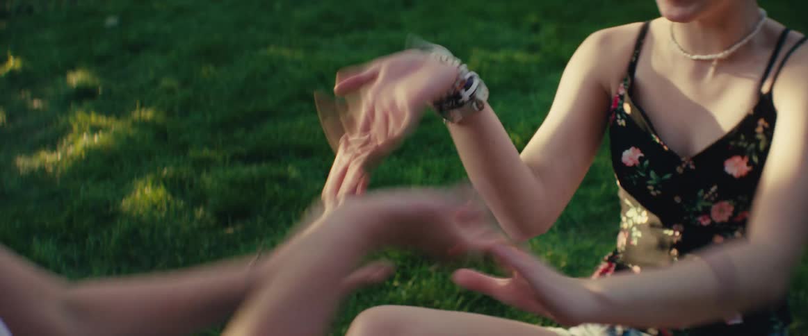 Teenagers play a clapping game while sitting on the grass in a lawn on a summer day