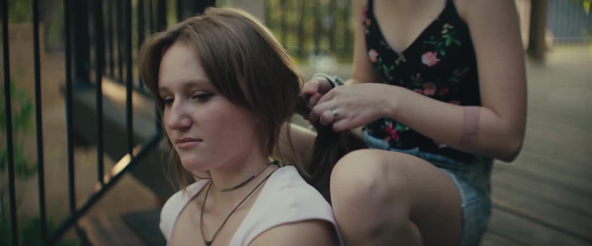 An older sister braids her younger sisters hair while sitting on outdoor stairs