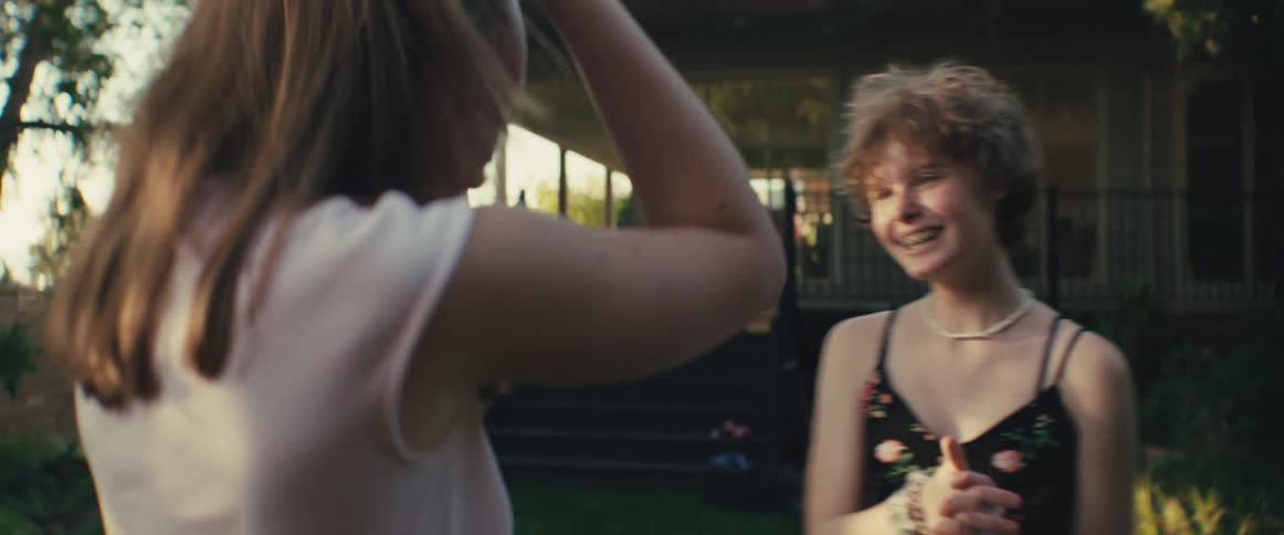 Two young women play a hand clapping game in a backyard at sunset