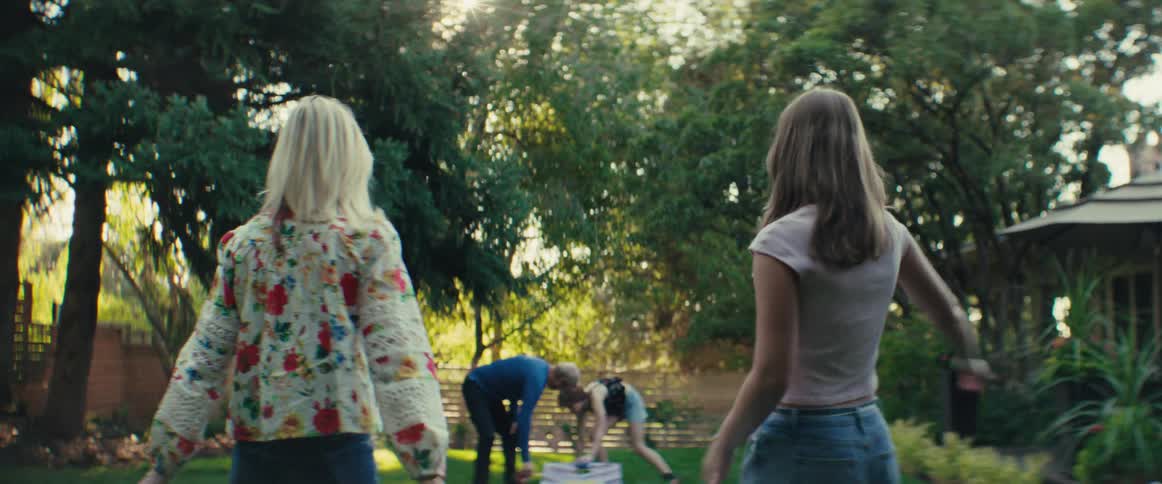 Two women hive five as other people pick up game pieces for an outdoor game