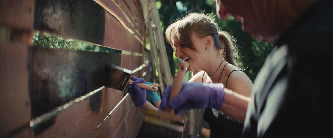 Dad and kids laughing as they paint a wood fence outdoors
