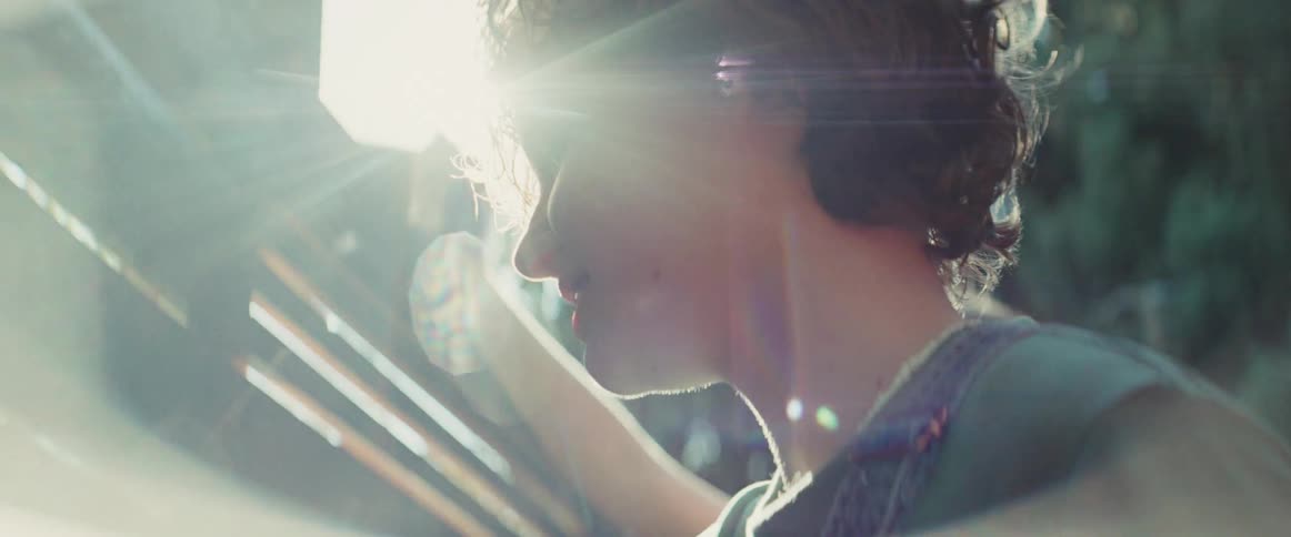 Person with curly hair interacting with wooden structure under bright sunset light