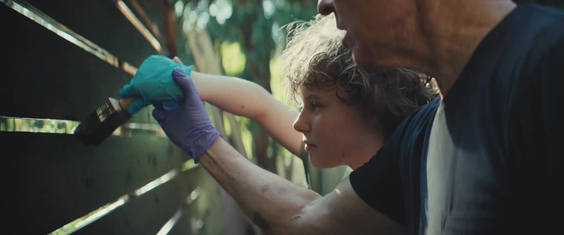 Child and adult paint a wooden fence under daylight