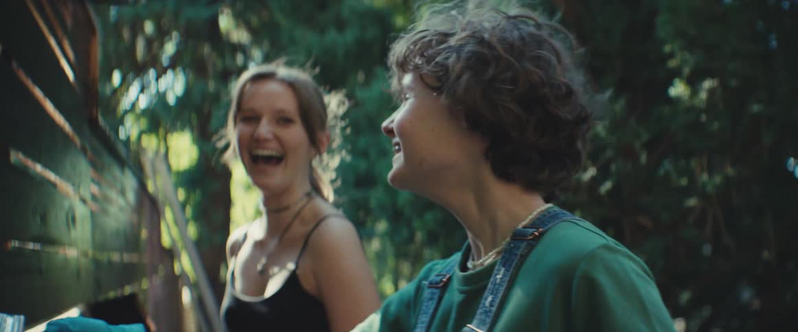 Two people laugh outdoors under the sunlight