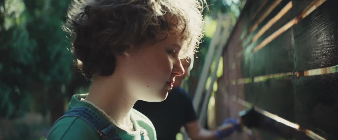 A child paints a wall alongside a middleaged man in the woods at midday