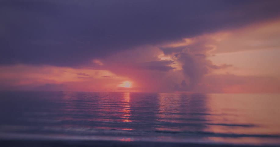 Waves roll into shore as the sun glows on the horizon