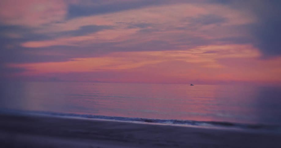 Ocean water stretches to the horizon under a cloudfilled sky a small boat sits near the center and waves gently break on the shoreline