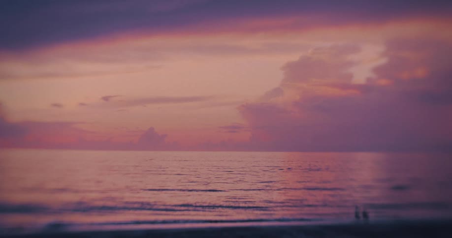 Two people walk on the beach as the sun goes down