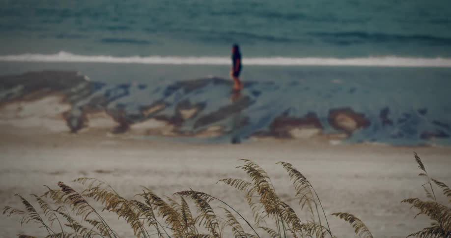 Two people walk along the waterline of a beach