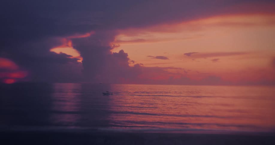 Vibrant sky reflects on calm sea with dense clouds at sunrise or sunset