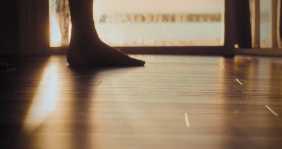 A low close view shows warm golden sunlight shining and reflecting brightly on a polished dark wood floor near a window with a soft lens flare