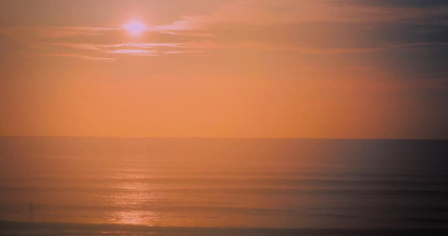 Waves roll into shore as the sun shines brightly through the clouds