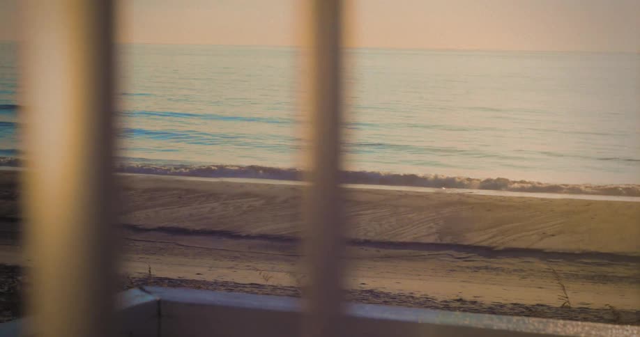 Gentle waves reach the sand at sunset seen through railings
