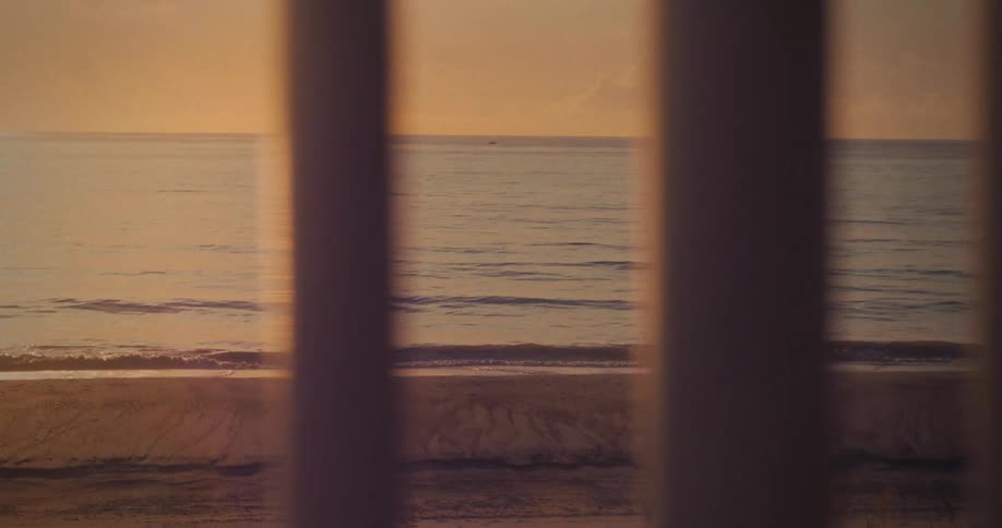 Ocean waves roll onto a sandy beach the view is framed by vertical pillars and the entire scene is illuminated by warm lowangle light