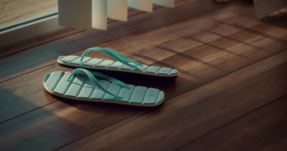 Pair of blue flipflops rests on a wooden floor lit by sunlight