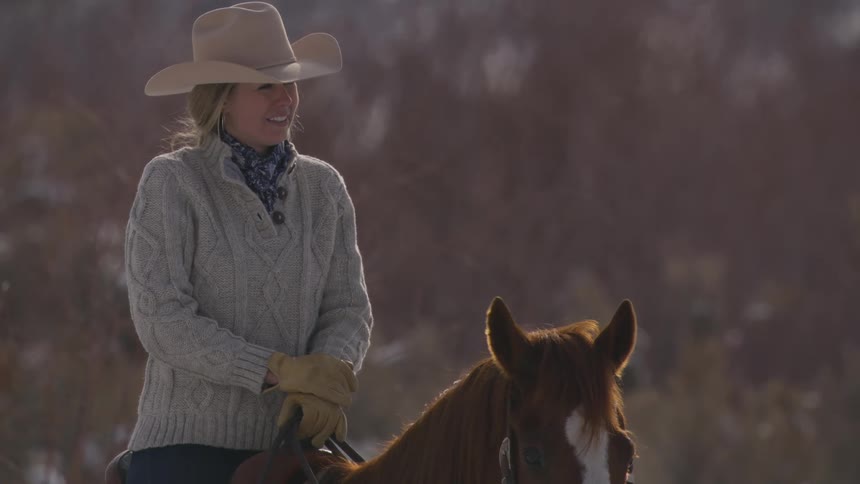 Woman wearing a cowboy hat rides a horse in a cold landscape