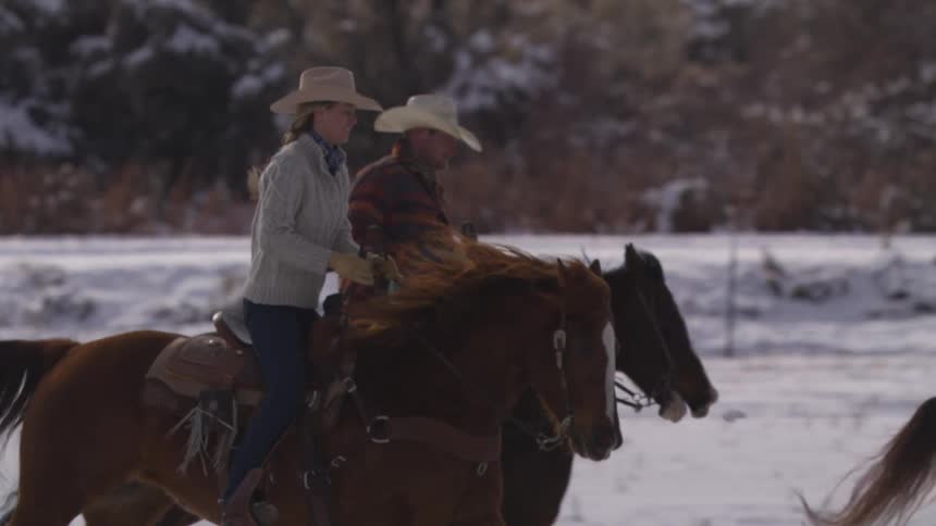 People are riding horses fast through a field covered in snow