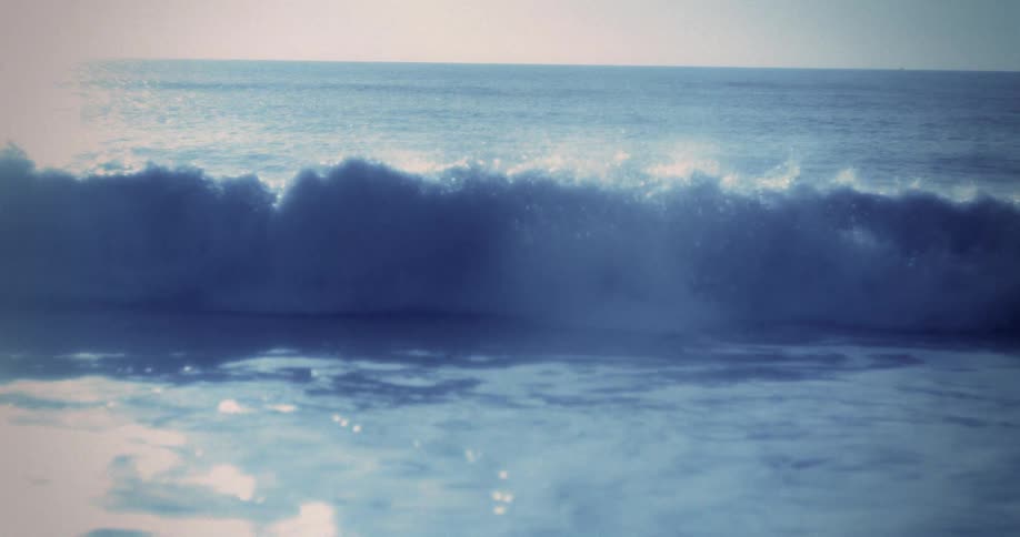 Waves gently crashing on shore with sunlight shimmering on deep blue sea