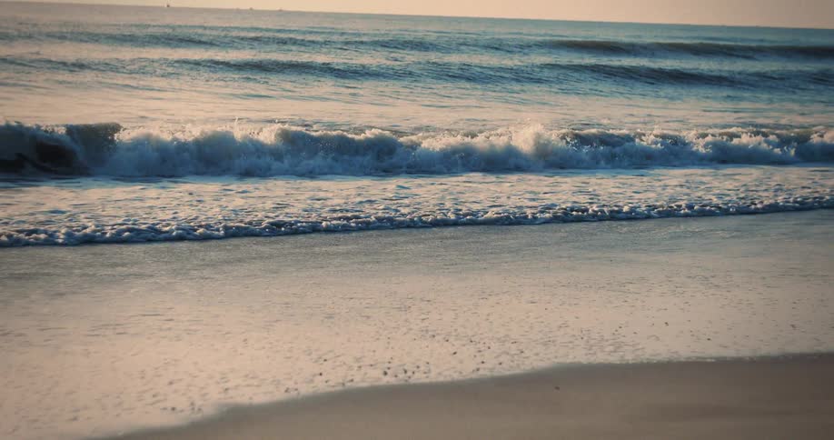 Gentle waves break on the sand under the golden light of sunset