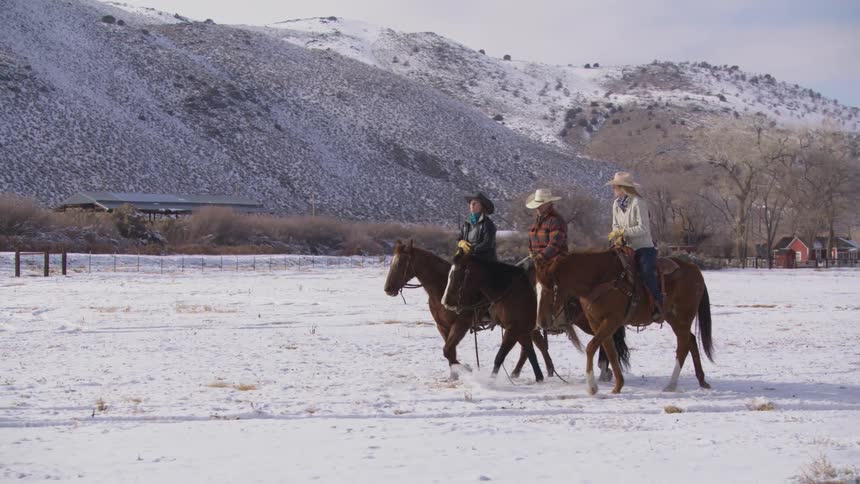 Three riders wearing cowboy hats riding across a snowcovered field