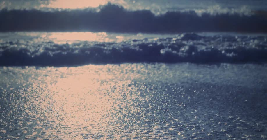 Ocean water reflects the light shining from a slightly tinted sky as waves foam on the beach