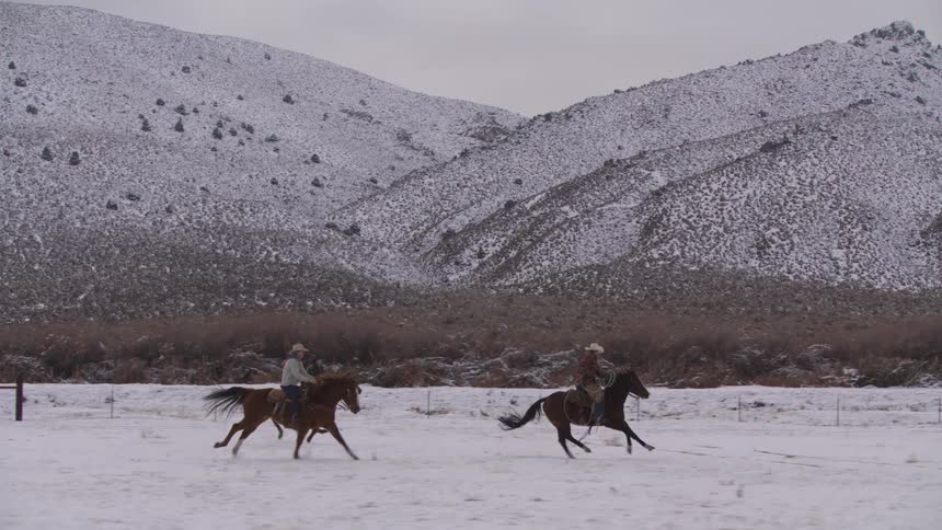 Three people riding their horses through the snow with a mountain landscape in the background