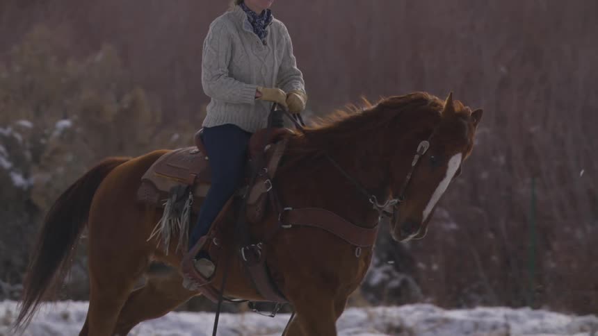 A young woman rides a horse on a ranch with snow covering the ground at midday