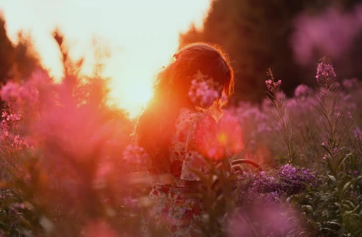 Woman in floral dress among wildflowers at sunset holding basket