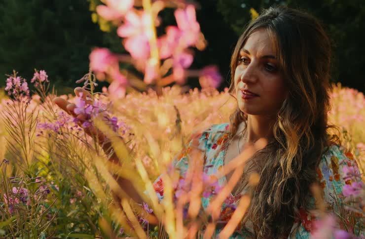 Woman among purple flowers gently observing one at sunset