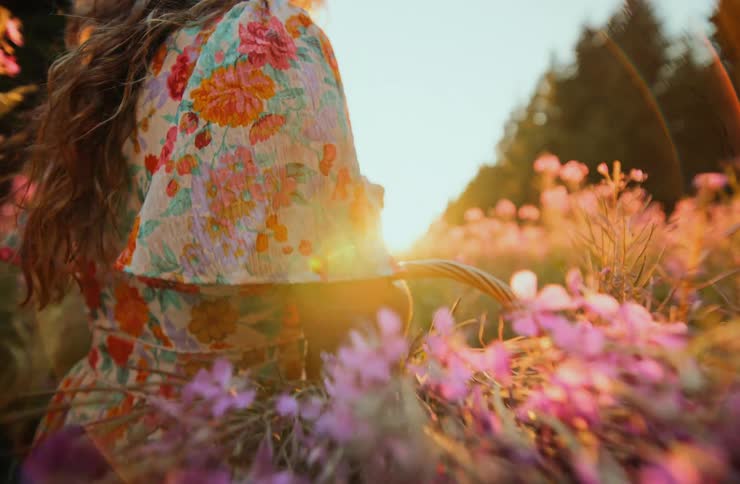 The woman carries a basket of flowers through the meadow