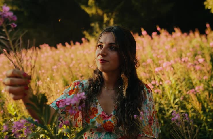 The woman holds up a flower on the field