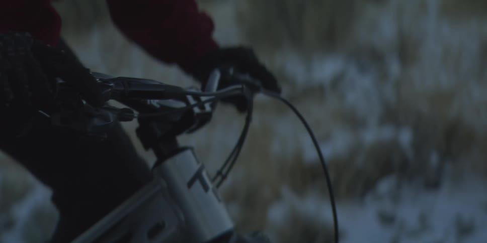 A person wearing gloves rides a bicycle in a dark setting the shot focuses on the handlebars and front frame and the bike moves forward