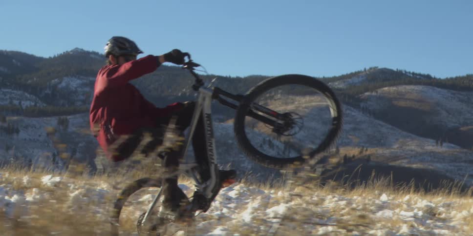 The man is doing a wheelie as he rides his bike past the mountains
