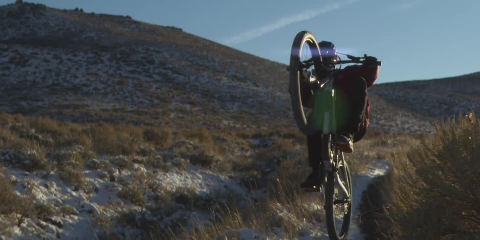 Cyclist rides along a trail between hills under a clear blue sky
