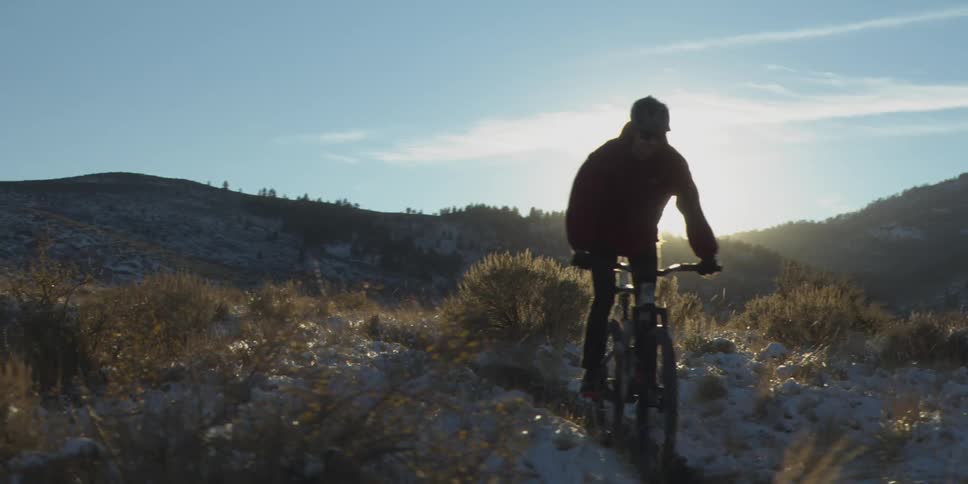 Cyclist rides along a snowy mountain trail under bright sunlight