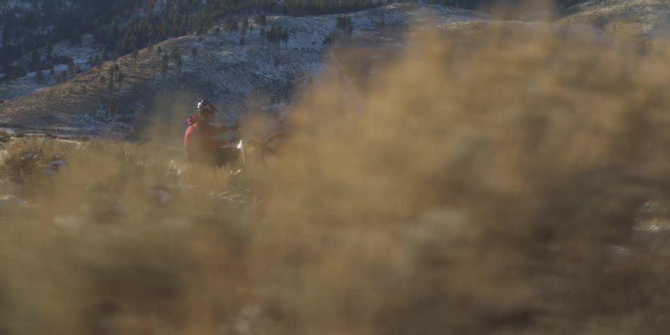 Cyclist performing a wheelie on a mountain trail with snow and dry vegetation