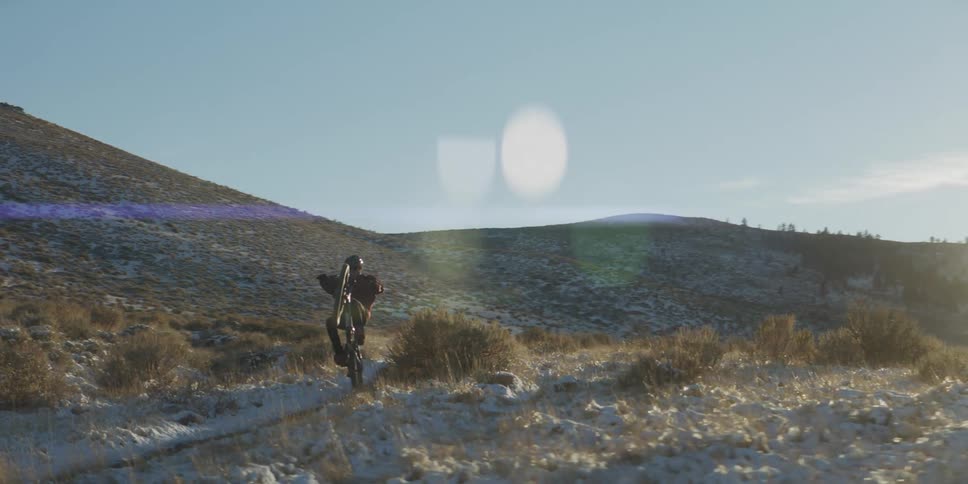 Man balances a bicycle on its rear wheel along a path near the hills on a sunny winter day