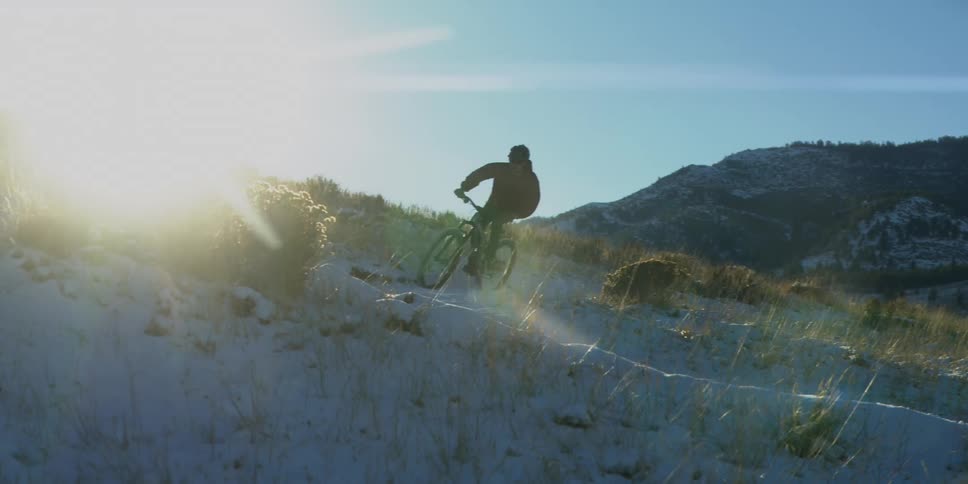 Cyclist rides a mountain bike along a snow covered slope on a sunny winter day