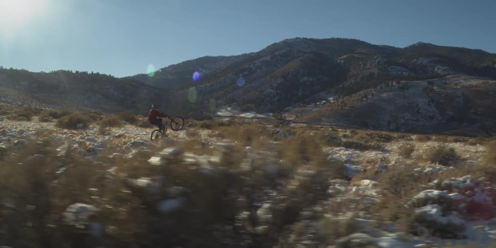 A man is popping a wheelie as he rides a bike through the desert in the mountains