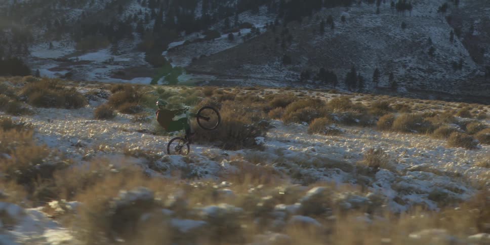 Cyclist performing a wheelie in an open field with snow and bushes