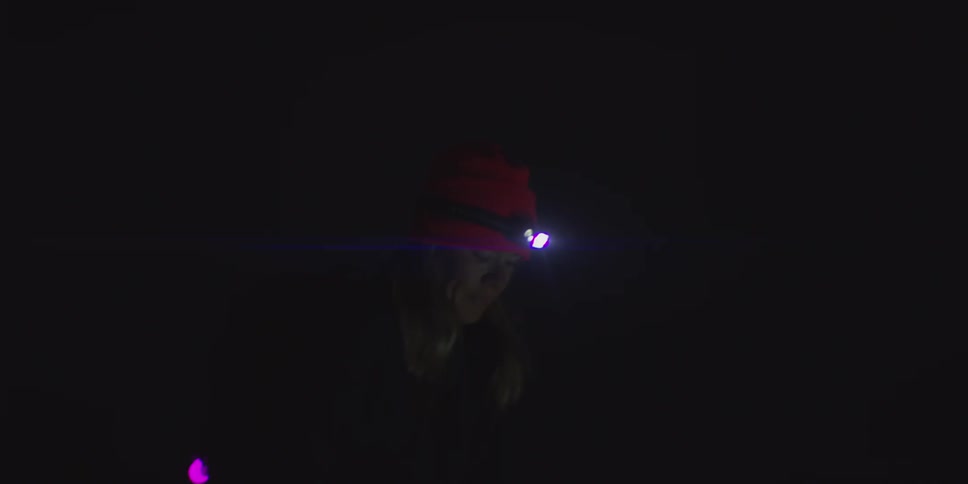 Woman wearing a headlamp uses walking sticks while walking at night