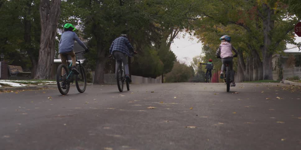 Group cyclists riding down residential street with fallen leaves and stop sign in background