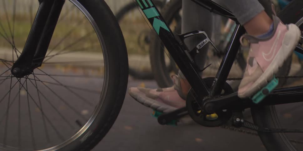 A cyclists pink nike sneaker pushes a pedal on a teal trimmed bike as nearby wheels spin