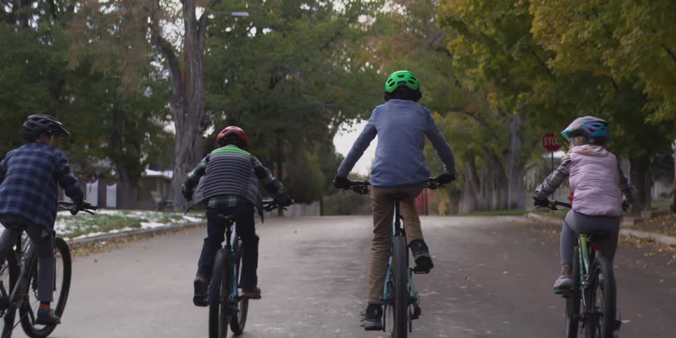 Children pedal their bicycles on a residential street past snow covered lawns