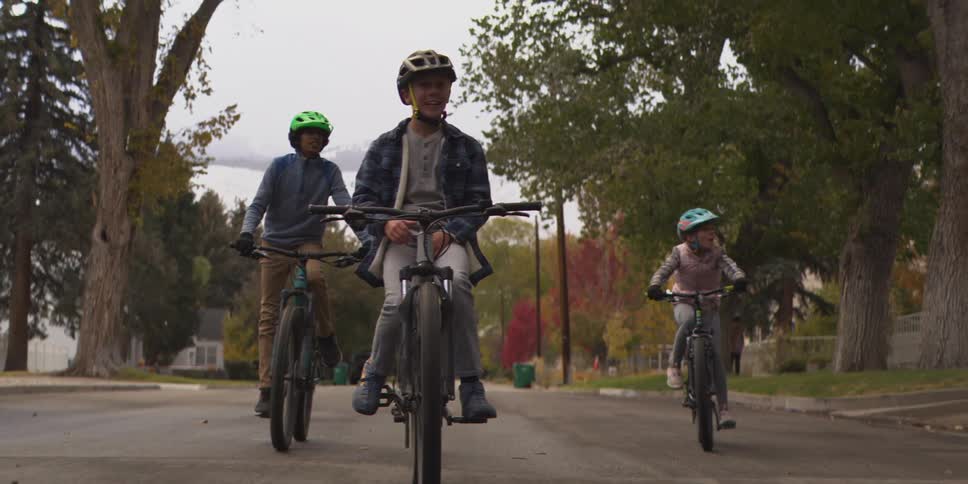 Children ride their bikes smiling along a treelined street