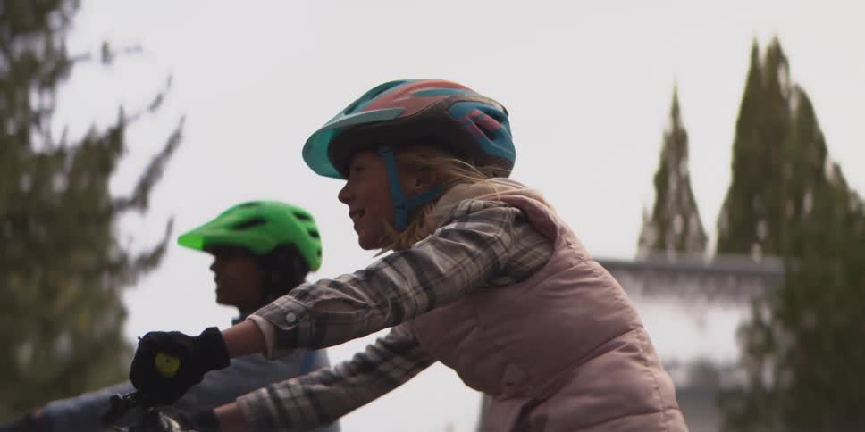 A cyclist in a pink vest and gray leggings pedals a trek bike alongside other helmeted riders