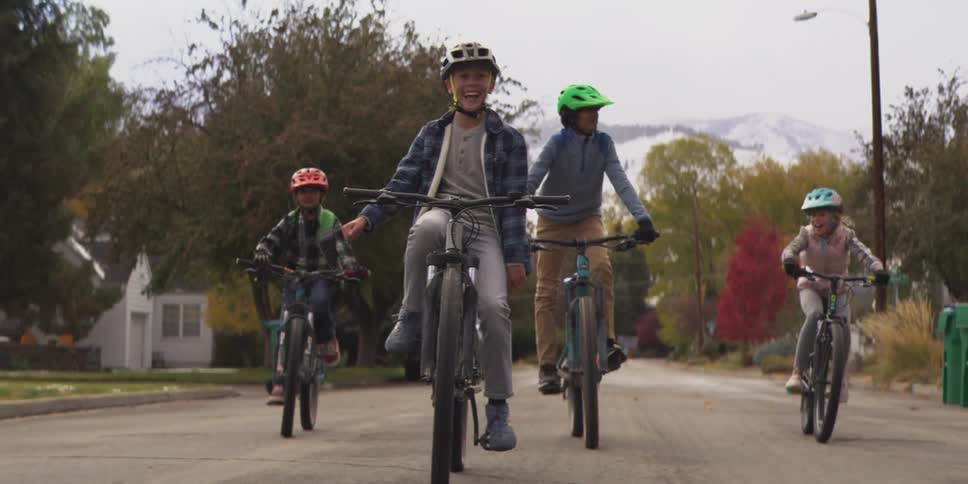 A group of kids with helmets on are riding bikes down a neighborhood street